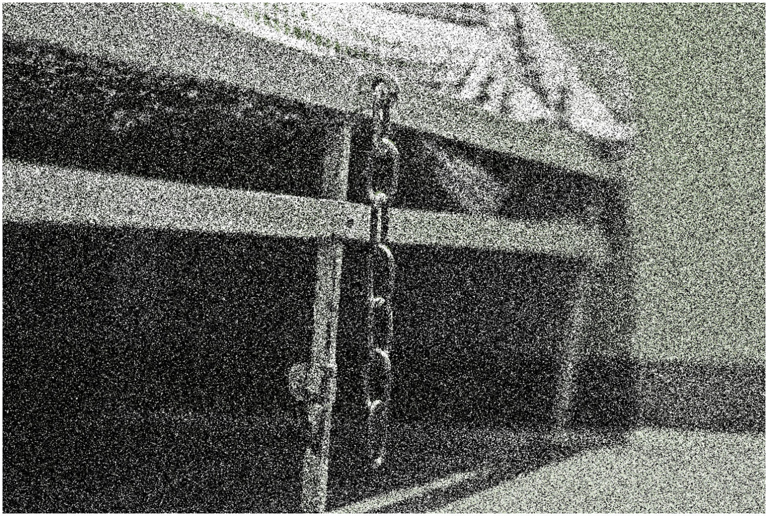 Raum mit Bett, an dem eine am Bettrahmen angeschraubte Kette zum Anketten von Gefangenen hängt, gobkörnig verfremdet.