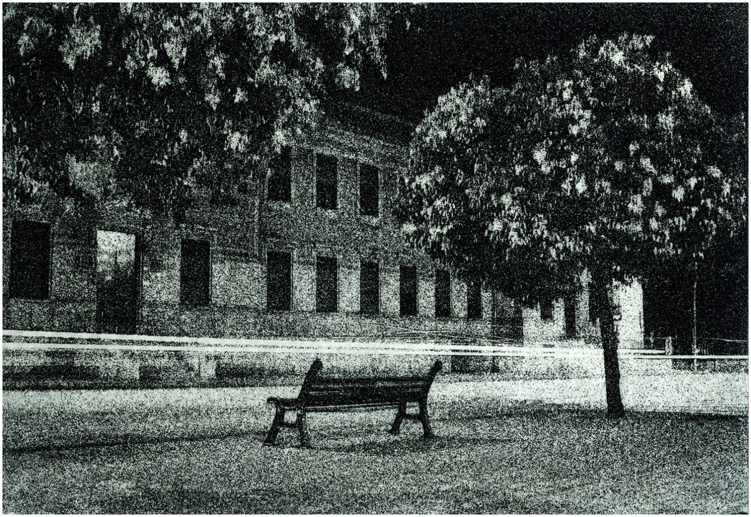 Fotoradierung: Nachtaufnahme einer Straße mit einer Parkbank und einem Baum vor einer Hausfassade