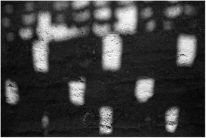 Schwarz-Weiß-Fotografie: Lichtflecken auf mit Steinen durchsetzten Sandboden