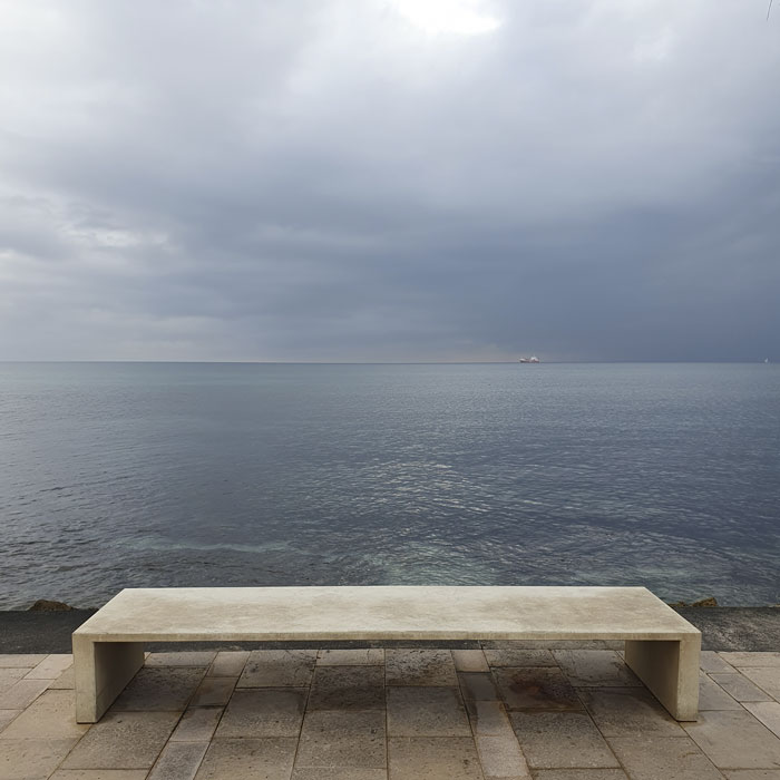Farbfotografie, die eine Bank mit dem Blick auf das Meer zeigt