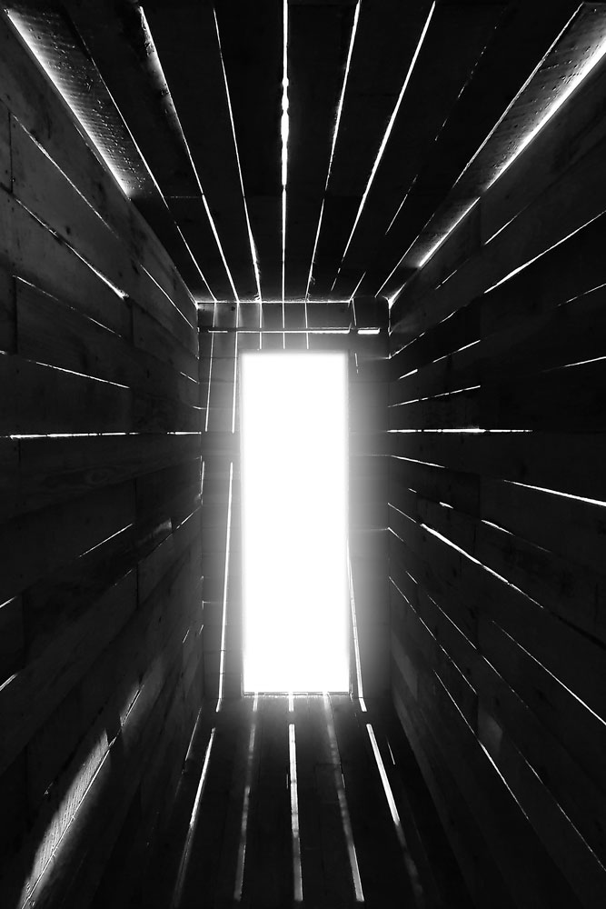 Schwarz-Weiß-Fotografie vom Innern eines Holzverschlags, dessen Tür offensteht